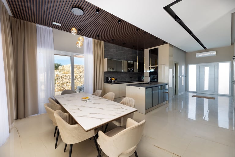 Modern open-concept kitchen and dining area with marble table, cream chairs, black cabinetry, and polished floor