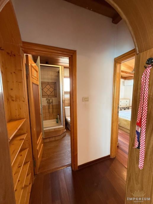 Interior hallway with wooden doors and frames, dark hardwood flooring, white walls, and bathroom visible through open doorway