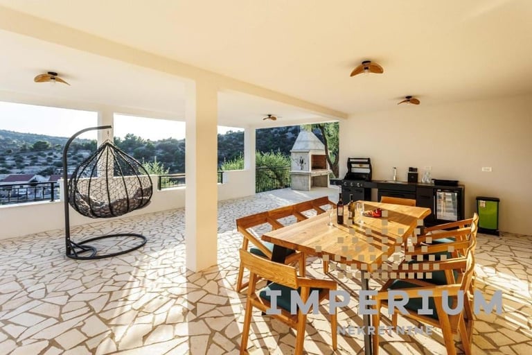 Bright open-plan dining area with wooden table, woven hanging chair, and glass doors opening to outdoor patio with mountain views