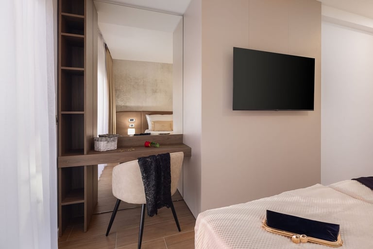 Modern hotel room with bed, desk with chair, wall-mounted TV, and built-in shelving storage