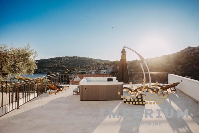 Modern rooftop terrace with hot tub, lounge chairs, and panoramic views of Mediterranean hills and water at sunset