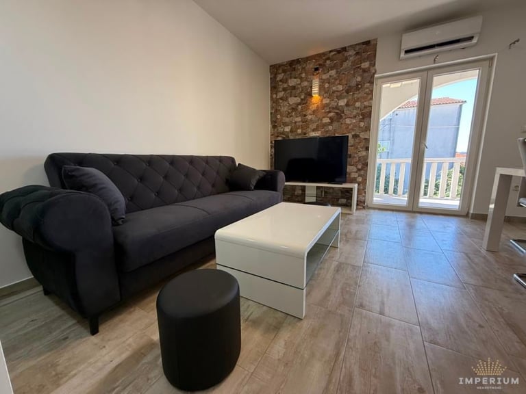Modern living room with black sofa, white coffee table, and TV mounted on brick accent wall with balcony doors