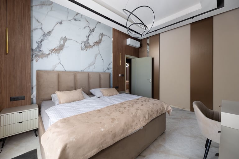 Modern bedroom with beige upholstered bed, marble accent wall, brown wood paneling, and contemporary furnishings in neutral tones