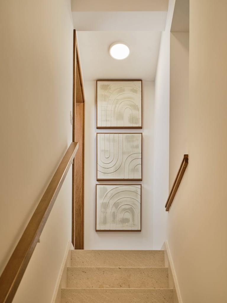 Modern stairwell with cream walls, wooden handrails, three framed geometric art prints, and recessed ceiling light