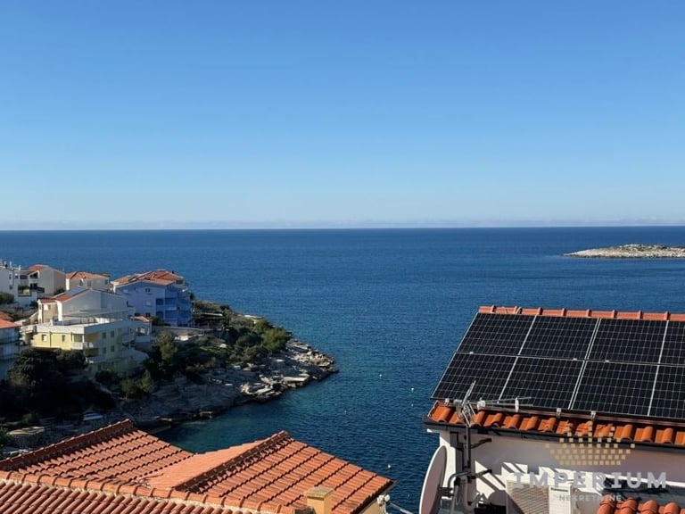 Solar panels on terracotta roof overlooking Mediterranean coastal town with blue sea and buildings