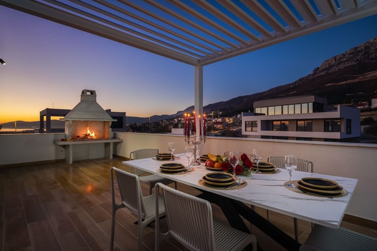 Modern rooftop terrace at sunset with dining table, fireplace, and panoramic mountain views at dusk