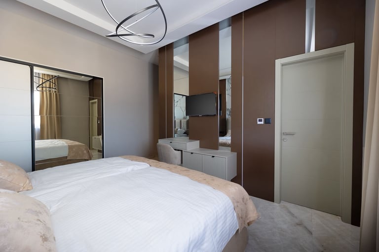 Modern bedroom with white bed, large mirror, brown and white accent wall, and contemporary furnishings