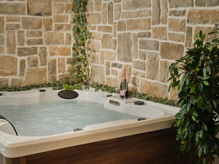 Outdoor hot tub with steaming water against a stone wall, decorated with ivy and plants