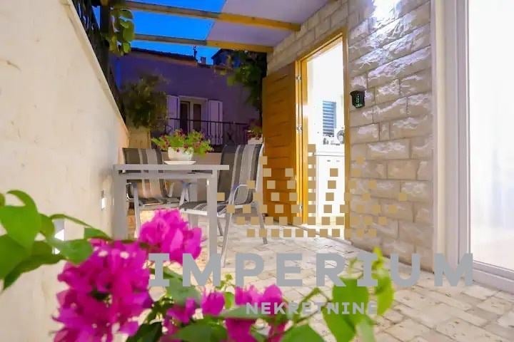 Modern patio with purple walls, wooden pergola, potted plants, dining furniture, and vibrant pink bougainvillea flowers in foreground