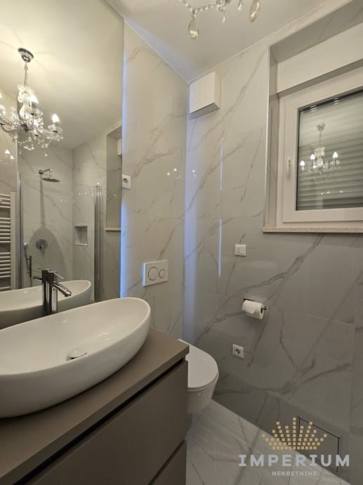 Modern bathroom with white oval sink, marble-tiled shower enclosure, wall-mounted fixtures, and contemporary lighting