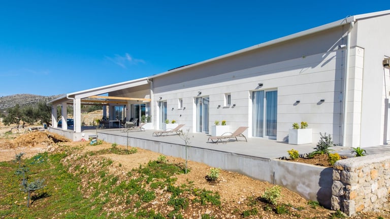 Modern white single-story house with covered porch, large windows, and stone foundation under clear blue sky