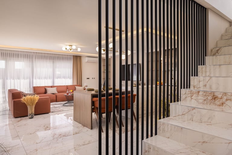 Modern living room with black vertical metal slats dividing the space, orange sectional sofa, marble flooring, and natural light from window