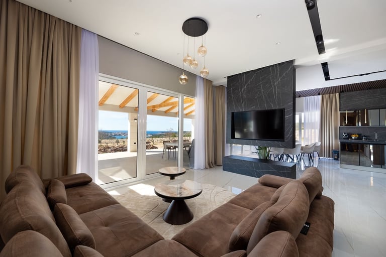 Modern luxury living room with brown curved sectional, mounted flat-screen TV, glass doors opening to a terrace with city views, and pendant lighting