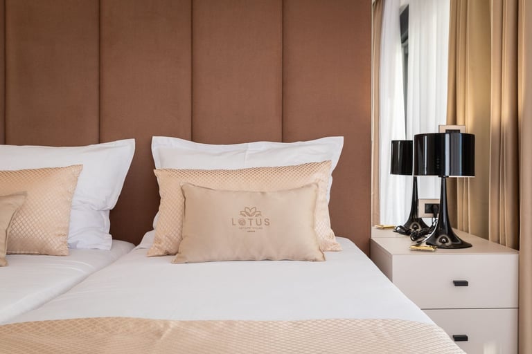 Modern bedroom with brown upholstered headboard, white bedding with beige pillows, and minimalist white nightstand with black lamp