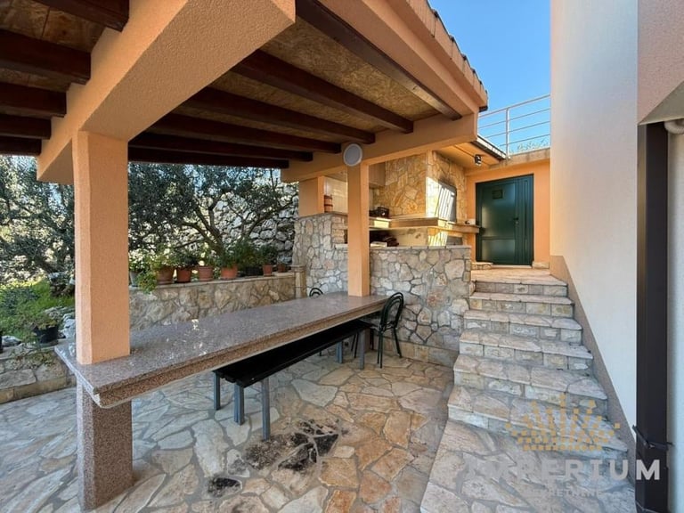 Covered patio with wooden beams, stone walls, and a long bench overlooking trees and landscape