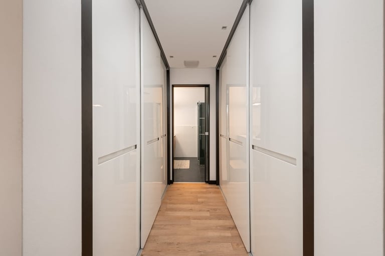 Modern hallway with white walls, dark trim, wooden floor, and built-in closets on both sides leading to a doorway