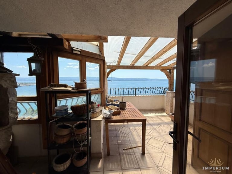 Modern seaside home interior with open terrace overlooking ocean, wooden pergola ceiling, and furnished patio area