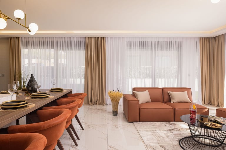 Modern open-plan interior with terracotta dining chairs, burnt orange sofa, neutral curtains, marble flooring, and contemporary lighting fixtures