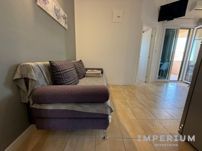 Modern living room with gray upholstered sofa, striped pillows, and blanket on tiled floor near glass patio doors