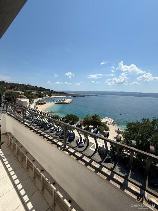 Coastal Mediterranean view from a terrace with ornate metal railing overlooking a turquoise bay and sandy beach
