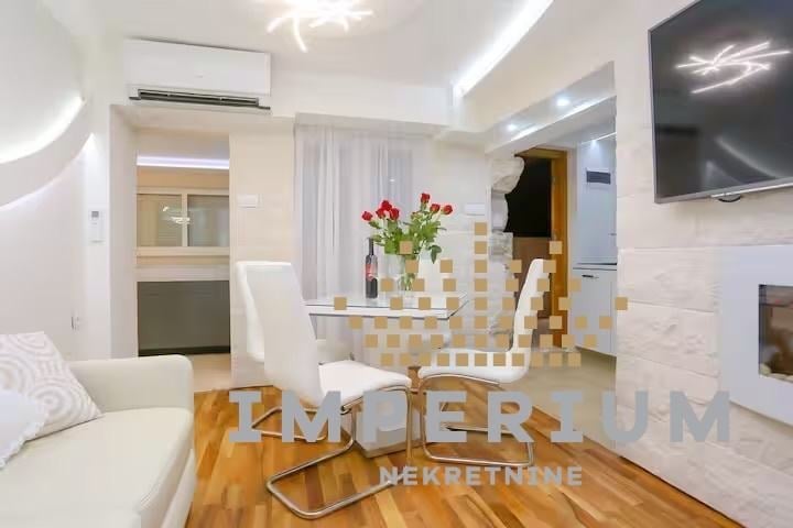 Modern studio apartment interior with white walls, wooden floor, dining area with flowers, kitchen counter, and modern lighting fixtures