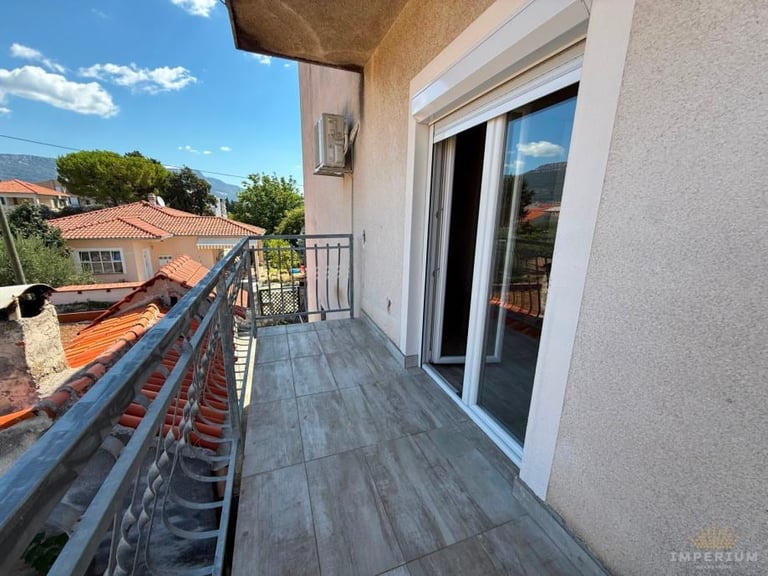 Modern balcony with dark wood flooring overlooking residential neighborhood with mountains under blue sky