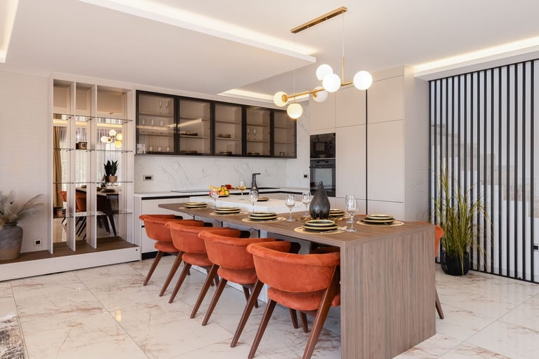 Modern kitchen with orange dining chairs at wooden island, white pendant lights, and black upper cabinets