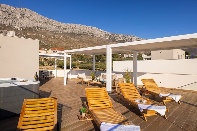 Modern rooftop terrace with yellow lounge chairs, wooden deck, white pergola, and mountain views under clear blue sky